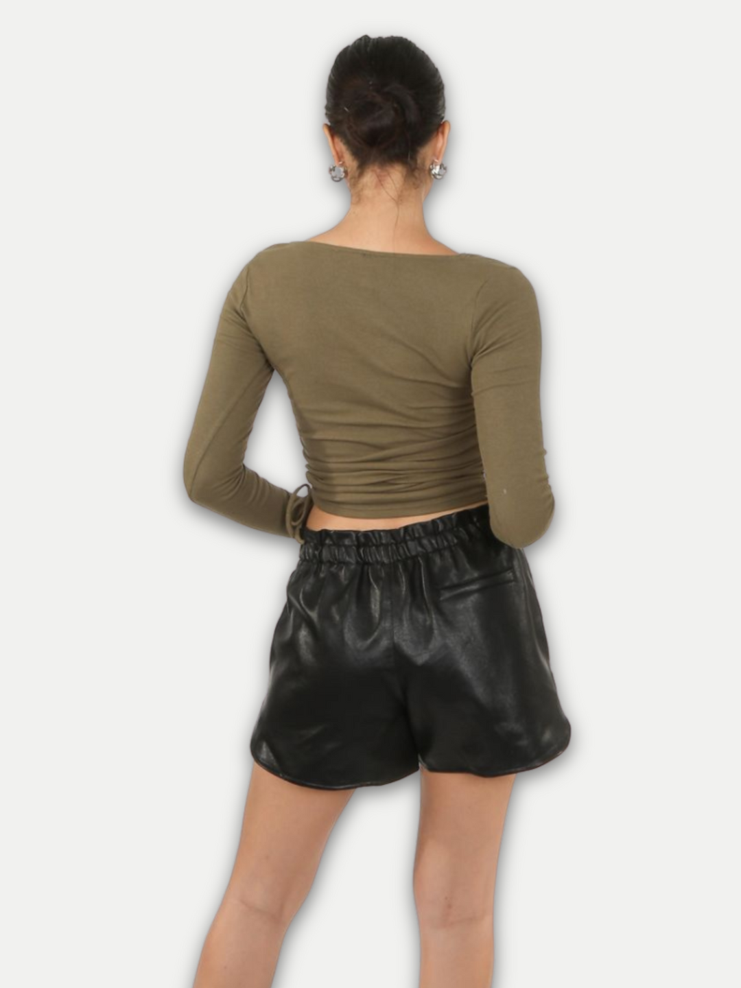  Model wears  pu leather running shorts, with front side pockets and a back pocket at the rear. The thick pu material demonstrates the high quality of the leather look shorts. Model stands with her back to the camera, the back pocket can be seen. 