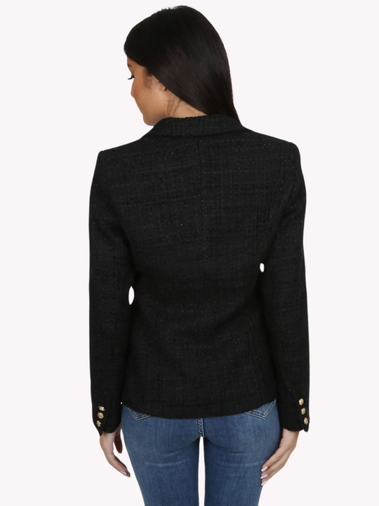 Model wears a black metallic yarn knitted double breasted blazer. The double breasted blazer has gold buttons at the front of the blazer and at the cuffs. Model stands with her back to the camera. The back of the blazer can be seen , including the gold buttons at the cuff.