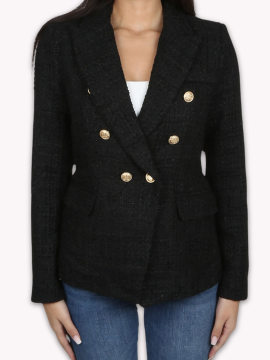 Model wears a black metallic yarn knitted double breasted blazer. The double breasted blazer has gold buttons at the front of the blazer and at the cuffs. She stands with her hands by her sides. 