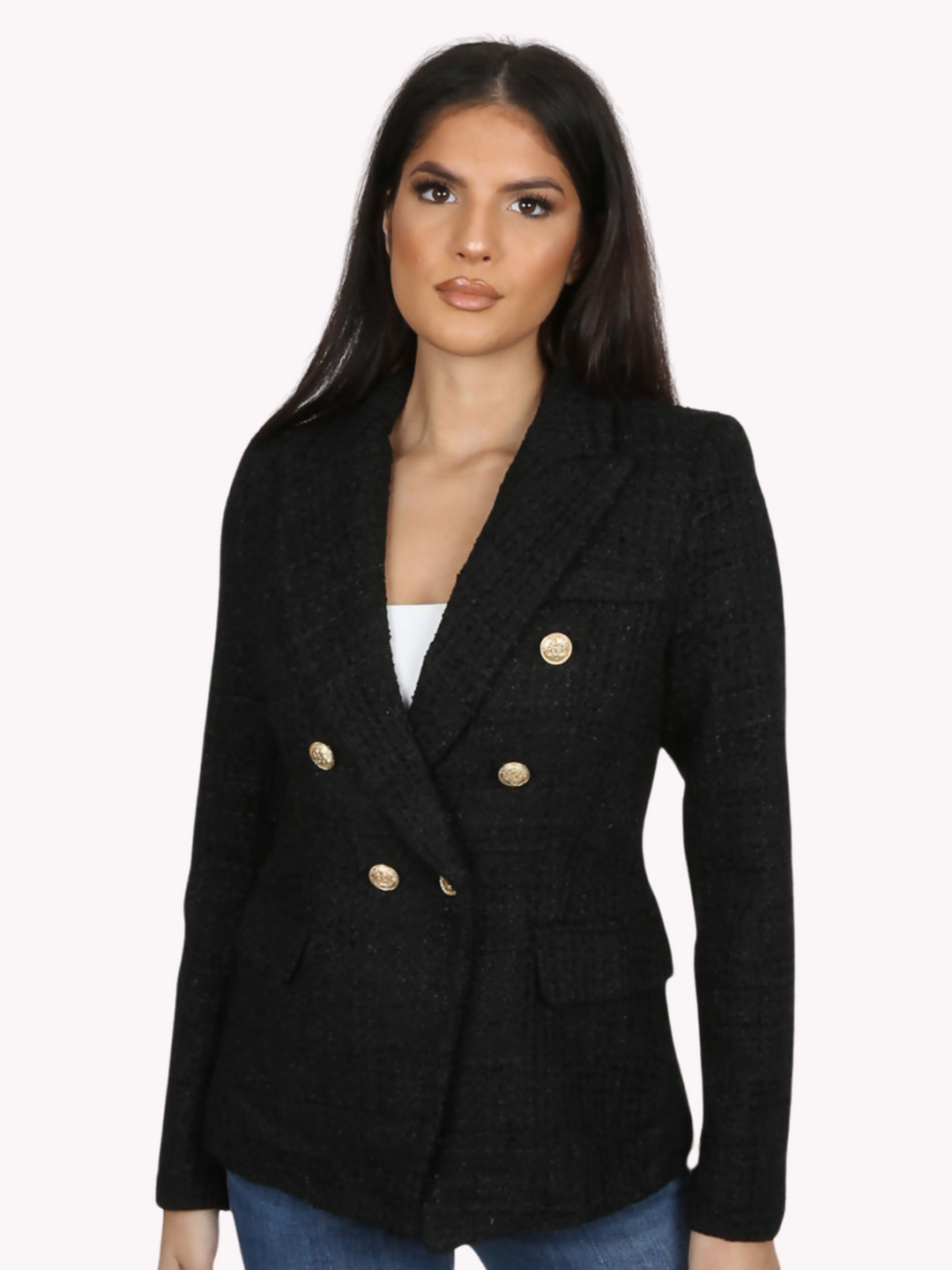 Model wears a black metallic yarn knitted double breasted blazer. The double breasted blazer has gold buttons at the front of the blazer and at the cuffs. Model faces forward with her hands by her sides.