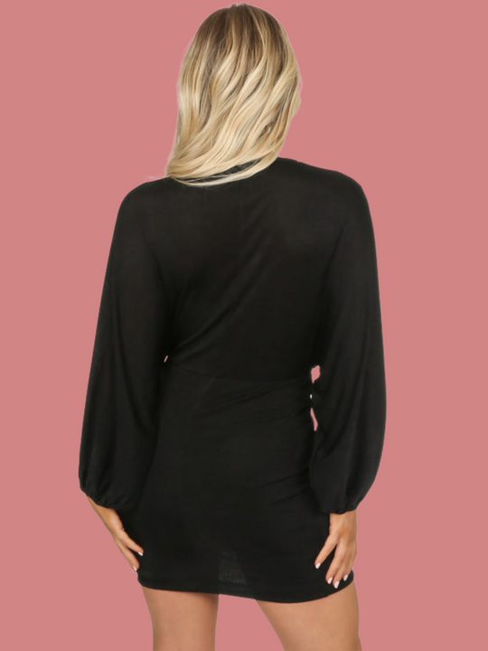 Model wears a black mini dress with adjustable plunging neckline, with long sleeved batwings. Model stands with her back to the camera and her arrms by her sides. The back of the dress can be seen.