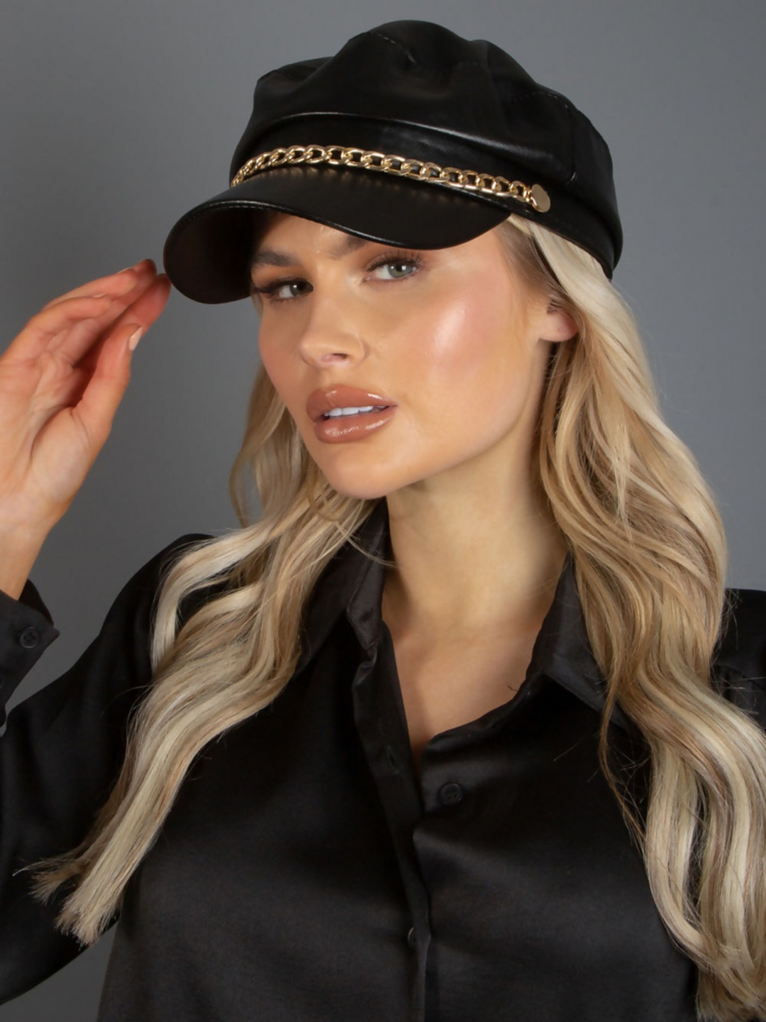 Mid length shot. Model wears a faux leather baker boy hat with gold chain detailing at the front. 