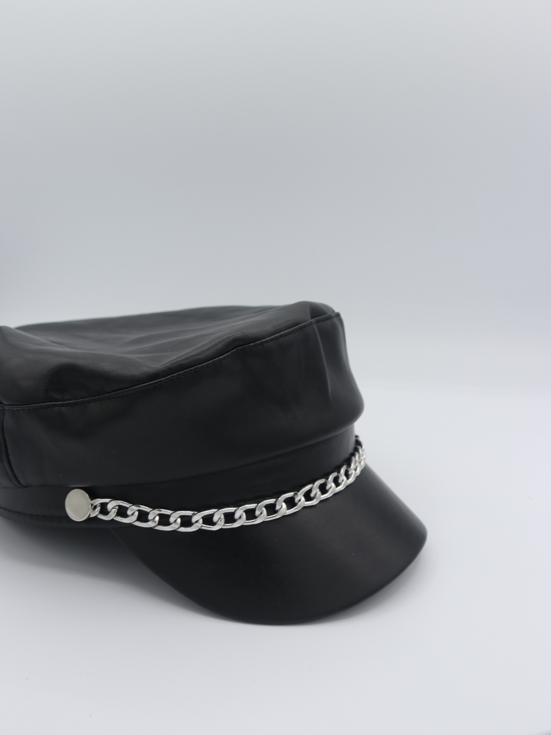 Side view of the baker boy PU hat with silver chain link at the front. The side profile and some of the front of the cap can be seen. 