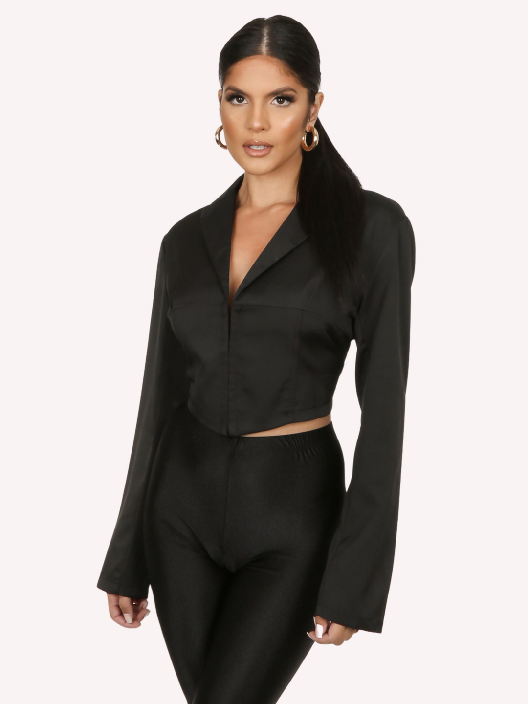 Model wears a black cropped shirt with a lapel, hook eye front closure and long sleeves that are wider at the cuffs.  Model faces the camera and turns at a a slight angle, model stands with her hands by her sides.