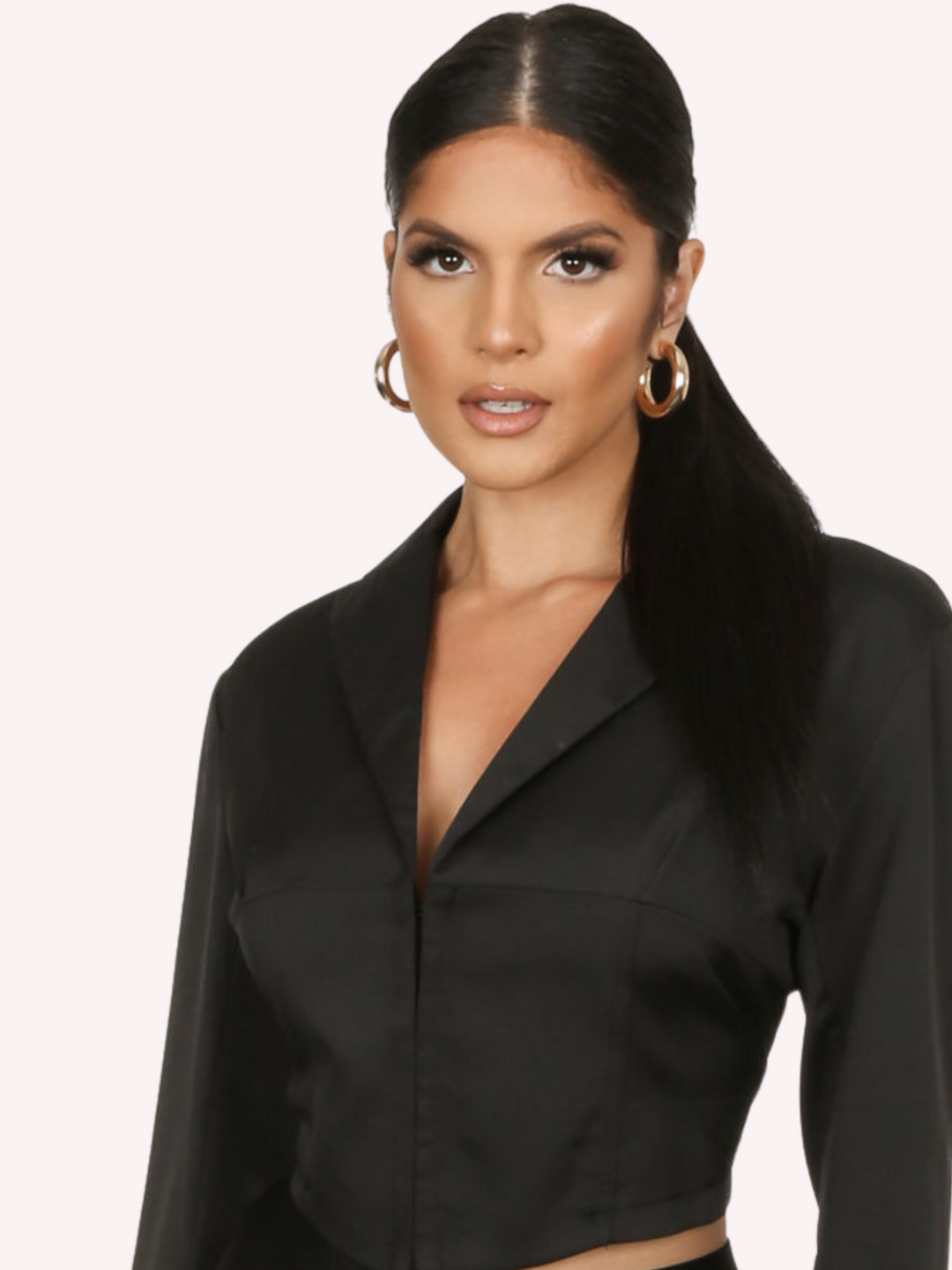 Close up of the shirt. Model wears a black cropped shirt with a lapel, hook eye front closure and long sleeves that are wider at the cuffs. 