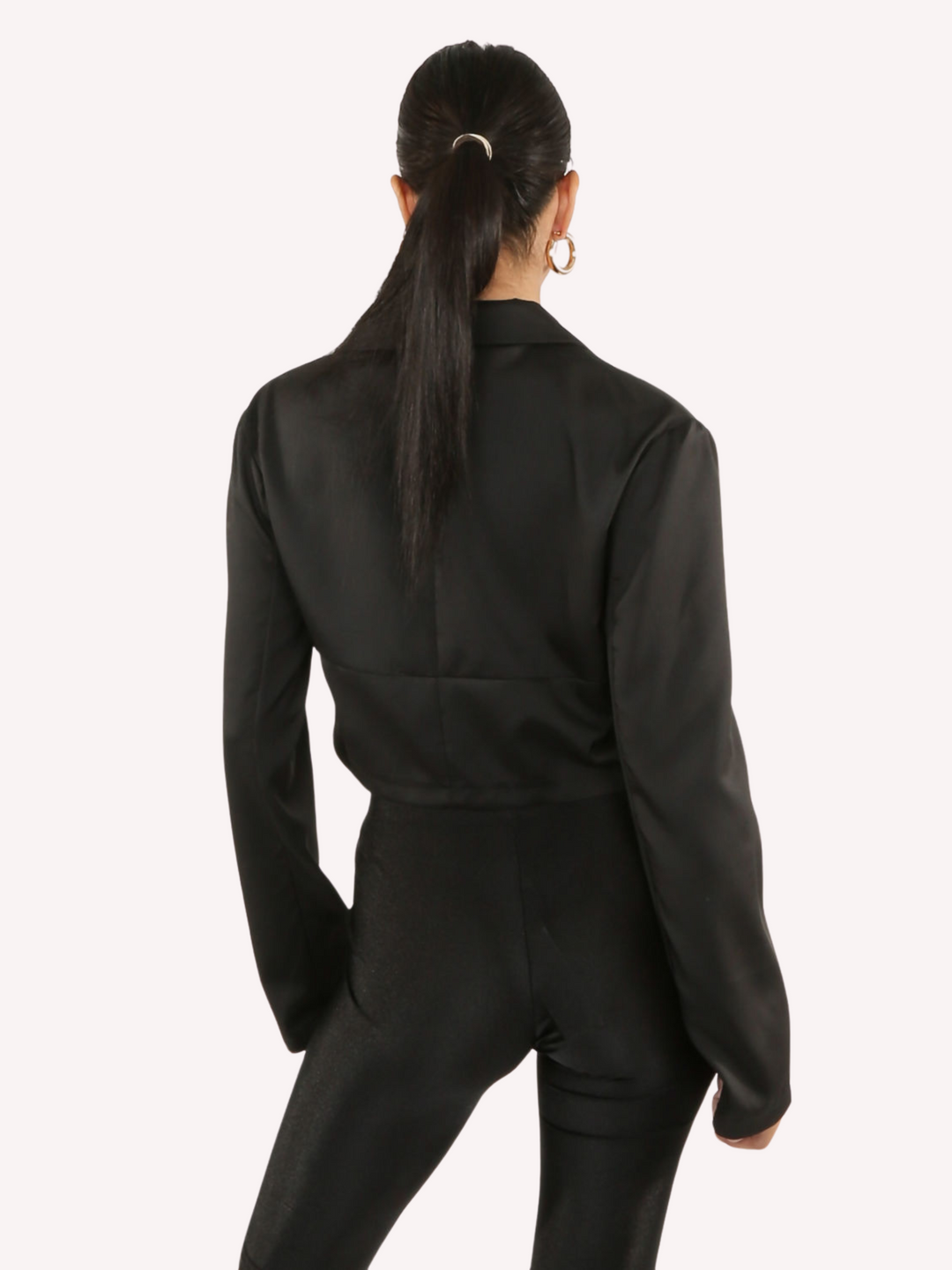 Model wears a black cropped shirt with a lapel, hook eye front closure and long sleeves that are wider at the cuffs.  Model stands with her back to the camera, the back o the shirt can be seen.