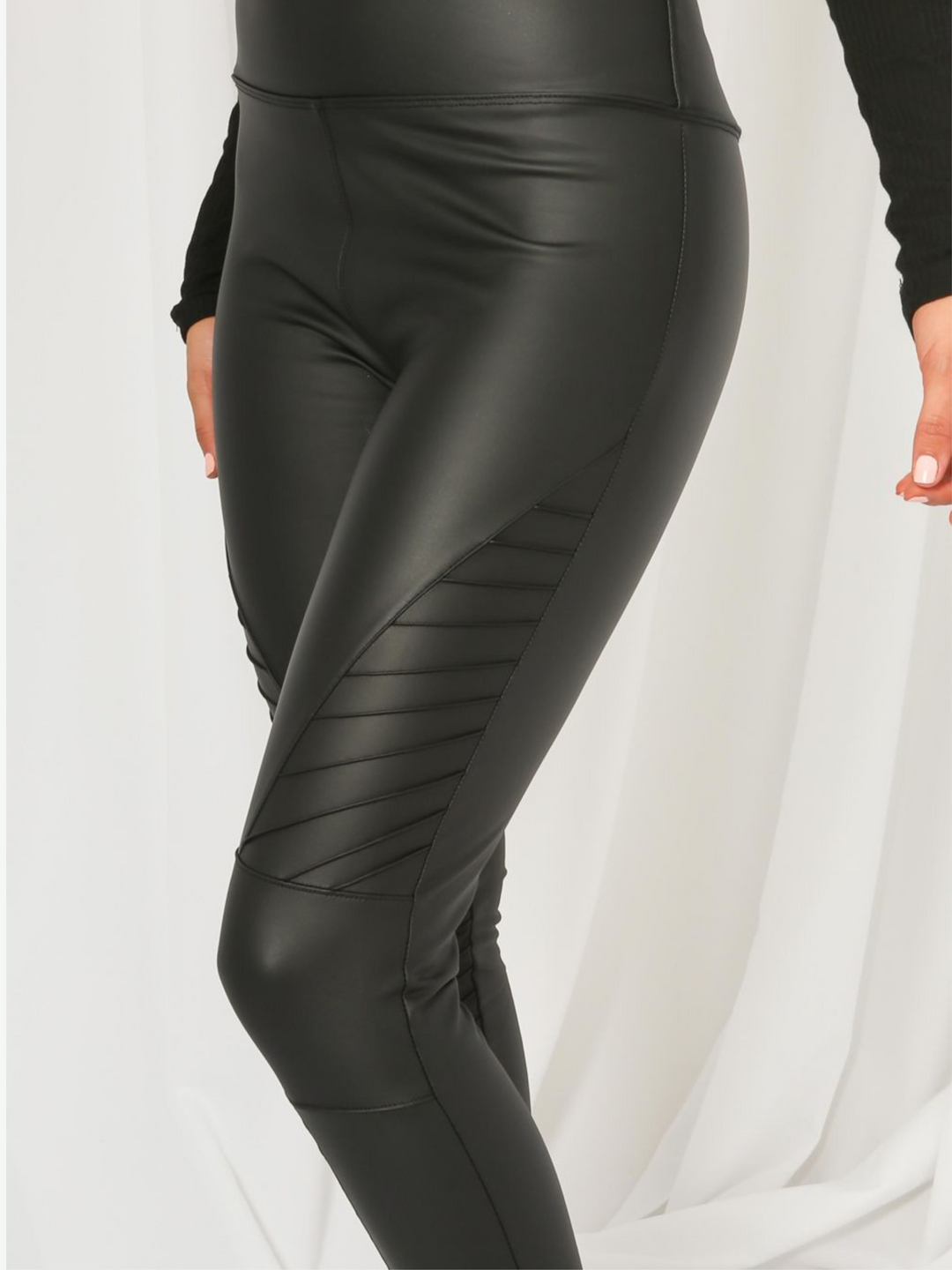 Model wears panelled high waisted leggings with a pu biker leggings design. Model stands to the side, the PU shin panel can be seen.