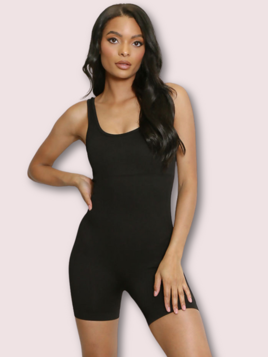 Model wears a black ribbed unitard jumpsuit with a scoop neck, waist control and open back. Model stands with one hand on her hip and one hand on her thigh.