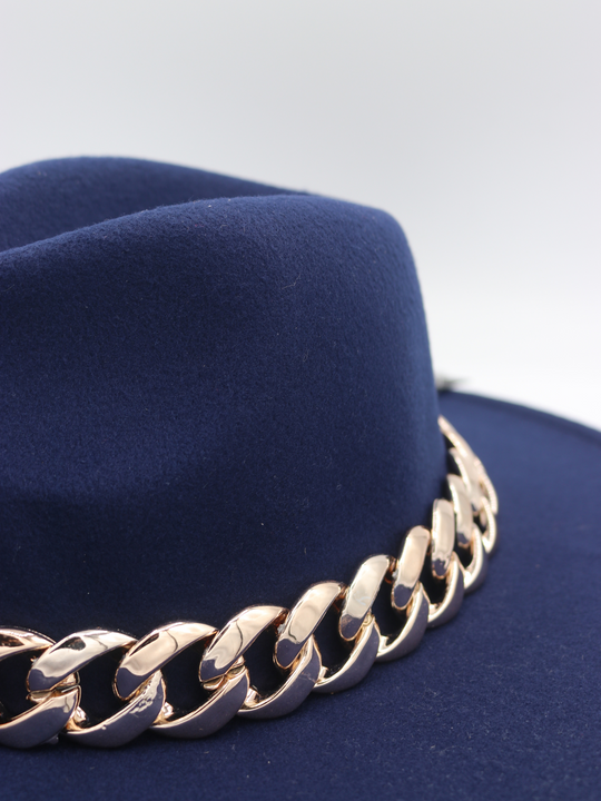 The side of the navy blue felt fedora hat can be seen. The chunky gold linked chain is also visible. 