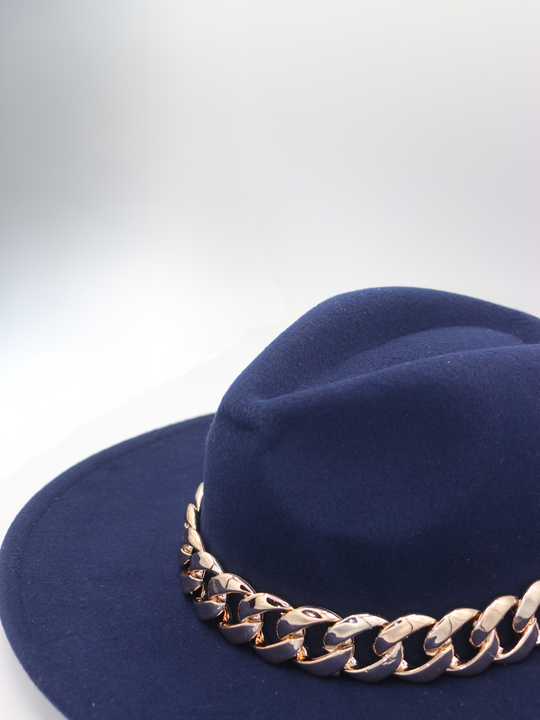 The  side of the navy felt fedora hat  with gold linked chunky chain detailing can be seen.  The top of the hat is also visible. 