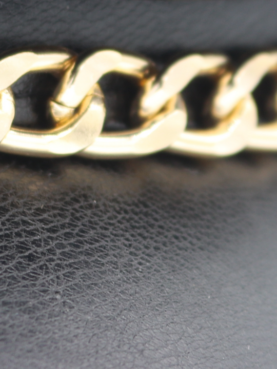 Close up of the gold chain on the faux leather cap. The picture shows the PU leather texture of the hat and the gold chain.