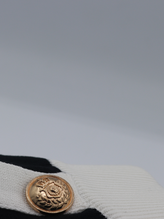 Close of gold military buttons on a black and white fine knit shorts set; with matching black and white crop top and and shorts and gold military buttons. One miltary button is visible. 