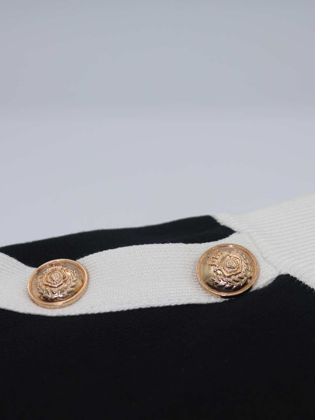 Close of gold military buttons on a black and white fine knit shorts set; with matching black and white crop top and and shorts and gold military buttons. One miltary button is visible.  Two miltary buttons are visble and are placed on the white block strip of the shorts.