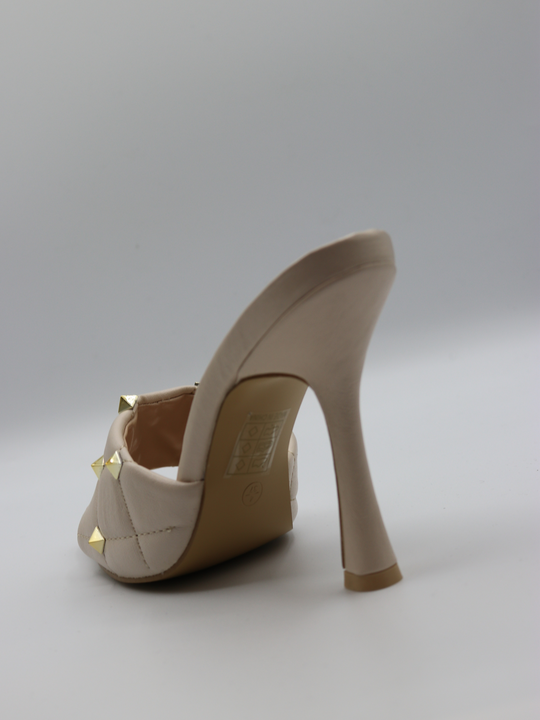 Cream quilted faux leather mule heels with gold studded heels. The back of the heel is visible, showing tghe cream slim heel. 