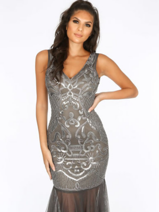 Mid length dress. Sequined grey maxi dress with sequined straps. Model holds one hand on his hip and one arm by her side.