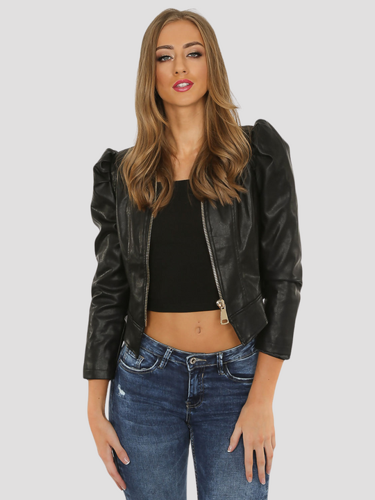 Mid length shot. Model wears a leather look faux leather cropped jacket with puffed shoulders and long sleeves. Model places both hands by her sides and wears the jacket open. The exposed front zip fastening is visible. 