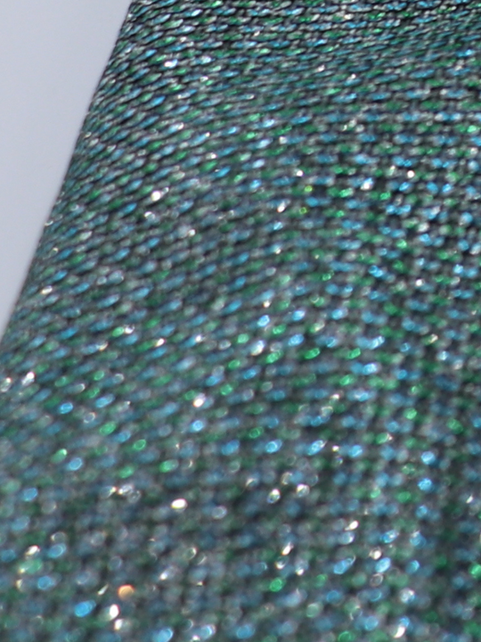 Closeup of green glitter micro mini dress with long sleeves. A closeup of the glitter material can be seen. 