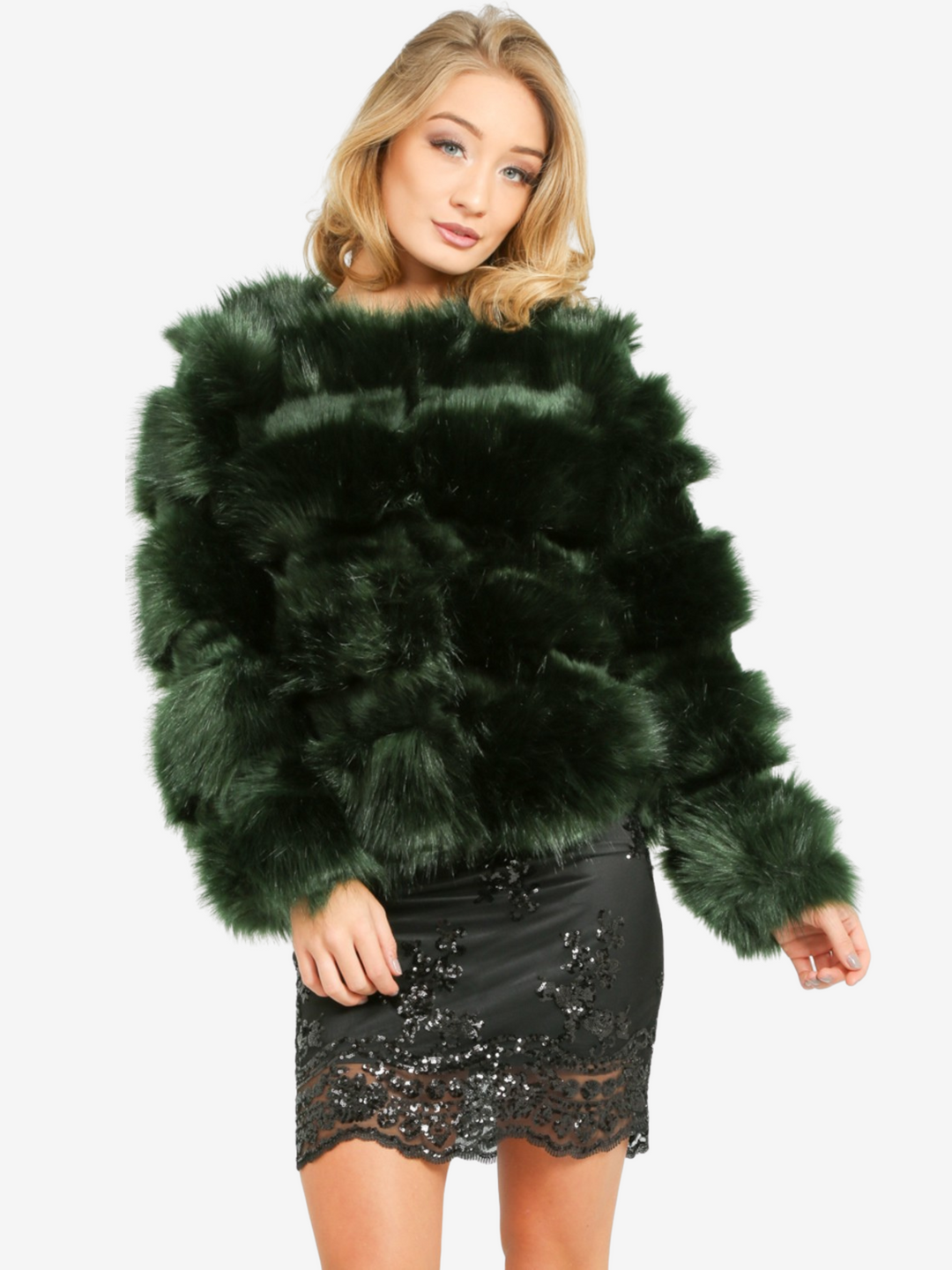 Model wears a soft faux fur long sleeve green jacket. The jacket has a front fastening and  satin like inner lining. Model wears the jacket closed, she is wearing a  black sequin dress. Mel stands with one hand on her thigh and the other by her side. 