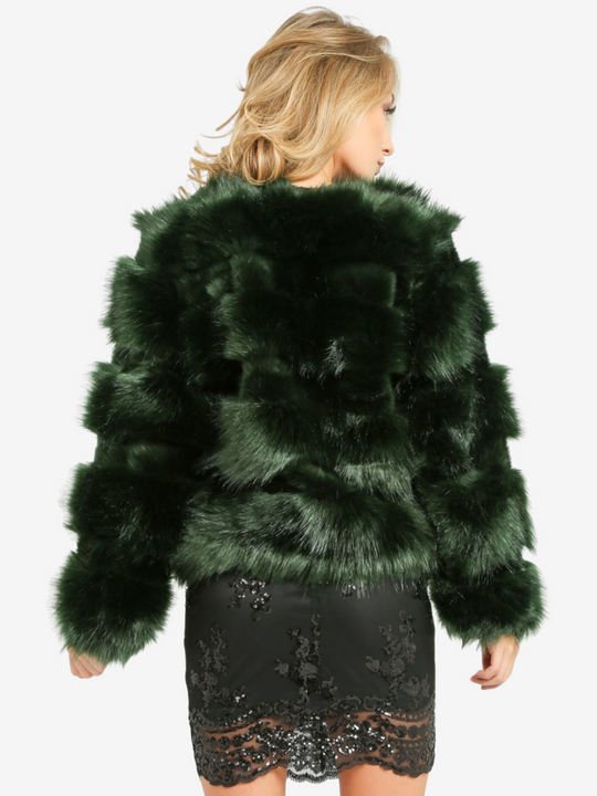 Model wears a soft faux fur long sleeve green jacket. The jacket has a front fastening and  satin like inner lining. Model  is wearing a  black sequin dress. Model stands with her back to the camera and her hands by her sides. 