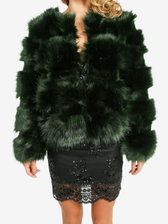 Mid length shot. Model wears a soft faux fur long sleeve green jacket. The jacket has a front fastening and  satin like inner lining. Model wears the jacket closed, she is wearing a  black sequin dress. She stands with her hands by her side. 