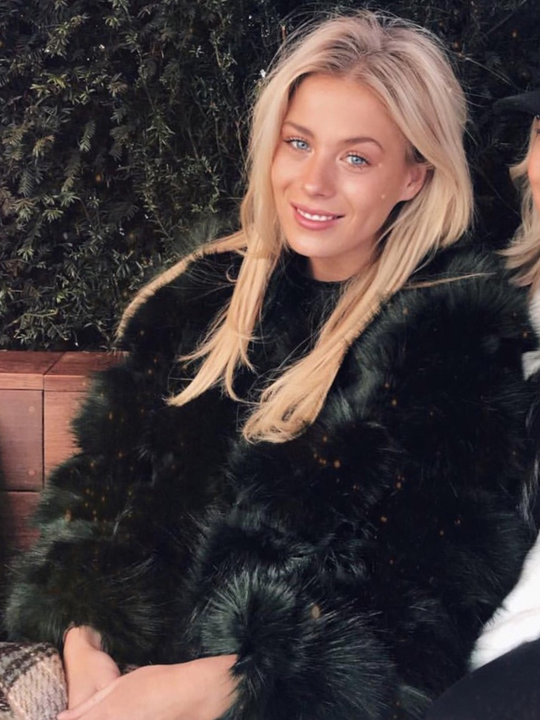 Model wears a soft faux fur long sleeve green jacket. The jacket has a front fastening and  satin like inner lining. Model wears the jacket closed and is sitting down. Model has blonde hair and blue eyes.  