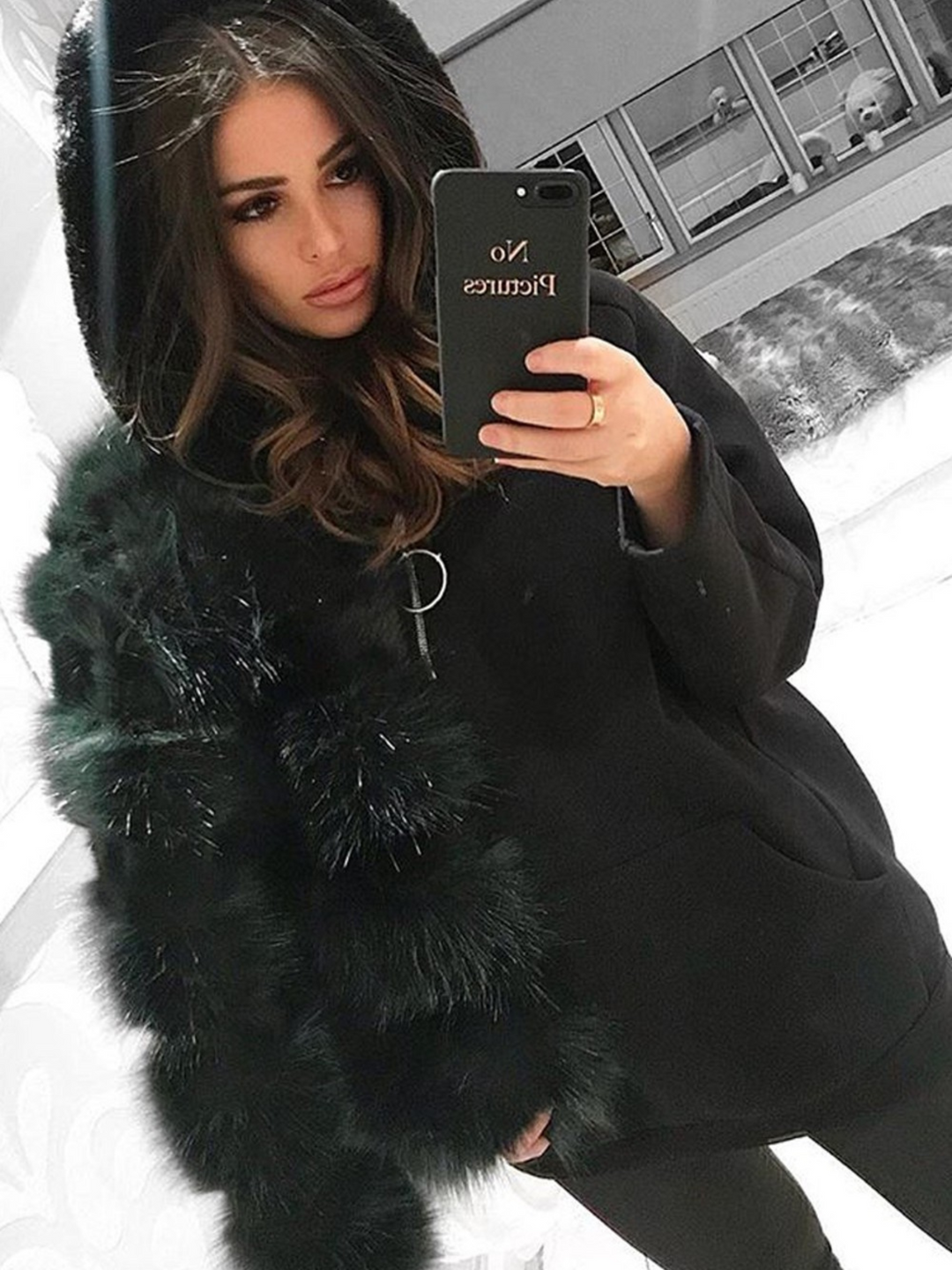 Model wears a soft faux fur long sleeve green jacket. The jacket has a front fastening and  satin like inner lining. Model wears the jacket on one shoulder. She os also wearing a black hoody and takes the picture with her phone.