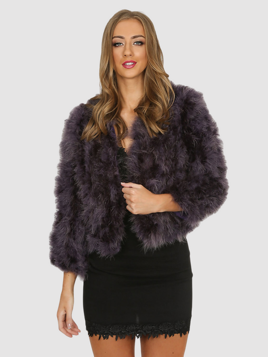 Model wears real ostrich feathered jacket with hook clasp fastening and long sleeves.  Model stands facing the camera, with one hand at the front and one hand by her side. 