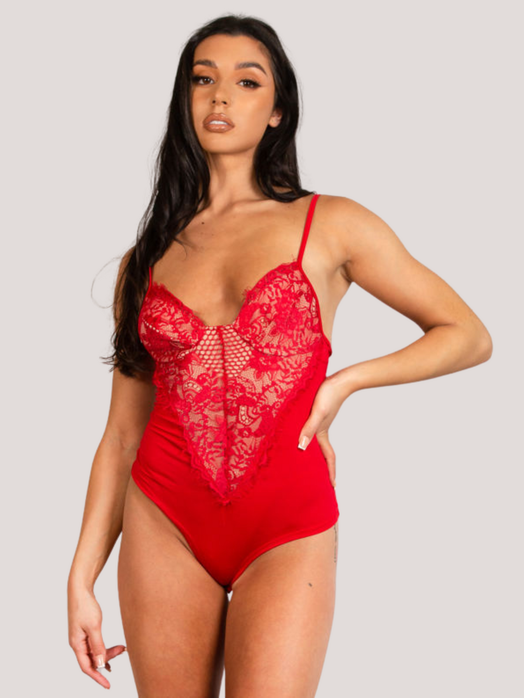 Model wears a red bodysuit with lace panel detailing. Model stand with one hand on her hip and the other by her side.