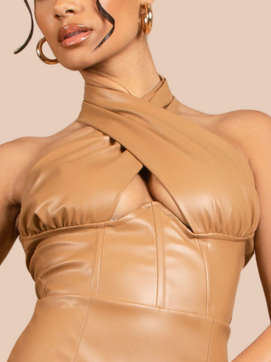 Model wears a faux leather tan coloured mini dress with cross over  halter neck design, panelled front, open back and back zip fastening. Closeup of the halter neck can be seen. 