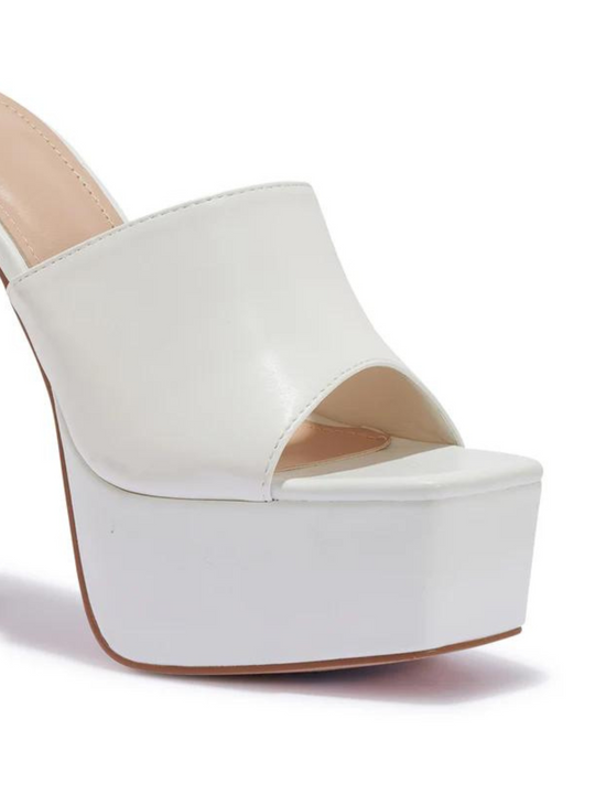 White heeled mules that have a thick platform base and stiletto shoes. The picture shows a close up of the side of the black platform, showing the thick platform base. 