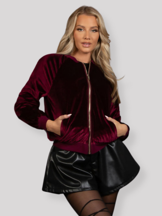 Model wears a red wine coloured velvet bomber jacket, that has long sleeves,  a front zip fastening and rounded neck.  Model faces forward and places her hands in the front zide pockets.