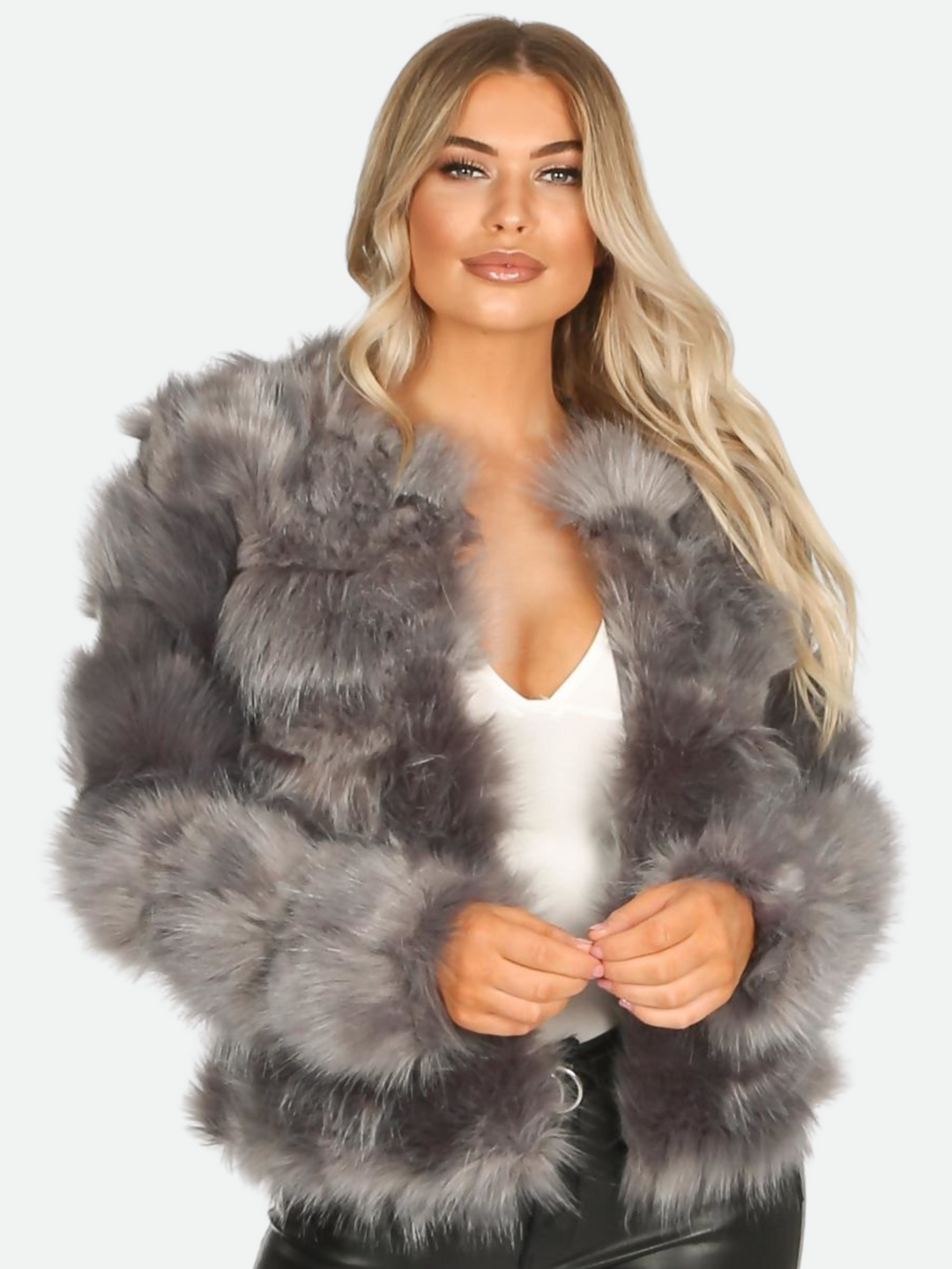 Close up of faux fur jacket. Model wears graphite grey faux fur jacket with long sleeves, rounded neck and front closure fastening.  Model looks directly into the camera with both hands in front.