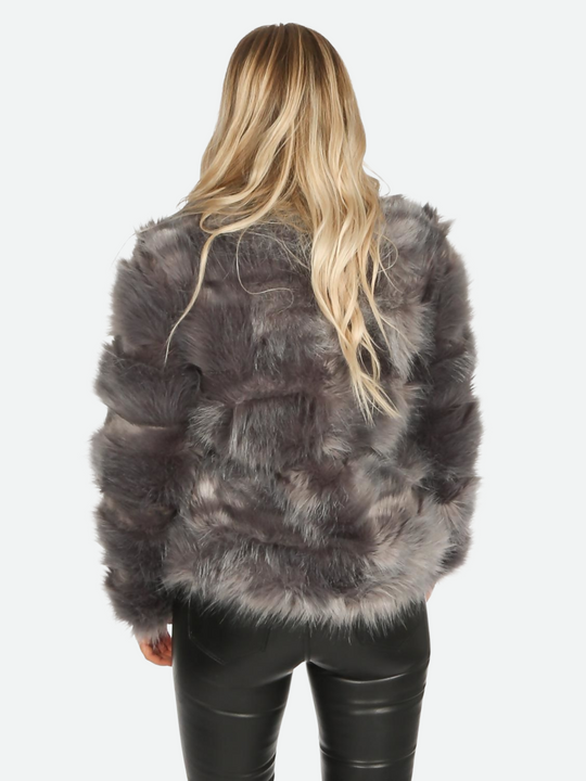 Model wears graphite grey faux fur jacket with long sleeves, rounded neck and front closure fastening.  Model stands  with her back to the camera. The  back of the faux fur jacket can be seen and the faux fur skinny jeans. 