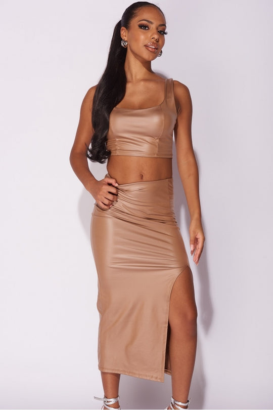 Model wears faux leather co-ordinated set in mocha. The crop top has a deep crew neck and the midi skirt has a thigh high split. Model stares directly into the camera with one arm on her hip amd one arm by her side. 